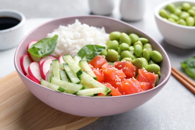 Photo of Poke bowl with salmon, edamame beans and vegetables on light grey table