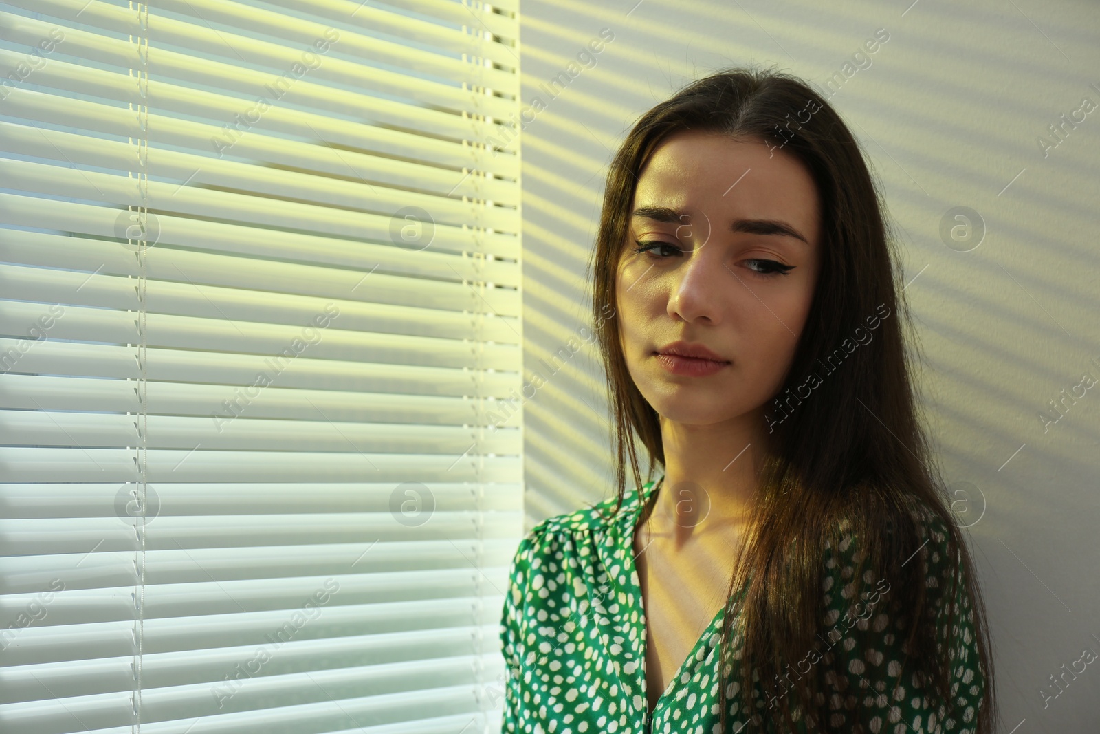 Photo of Young woman near window with Venetian blinds. Space for text