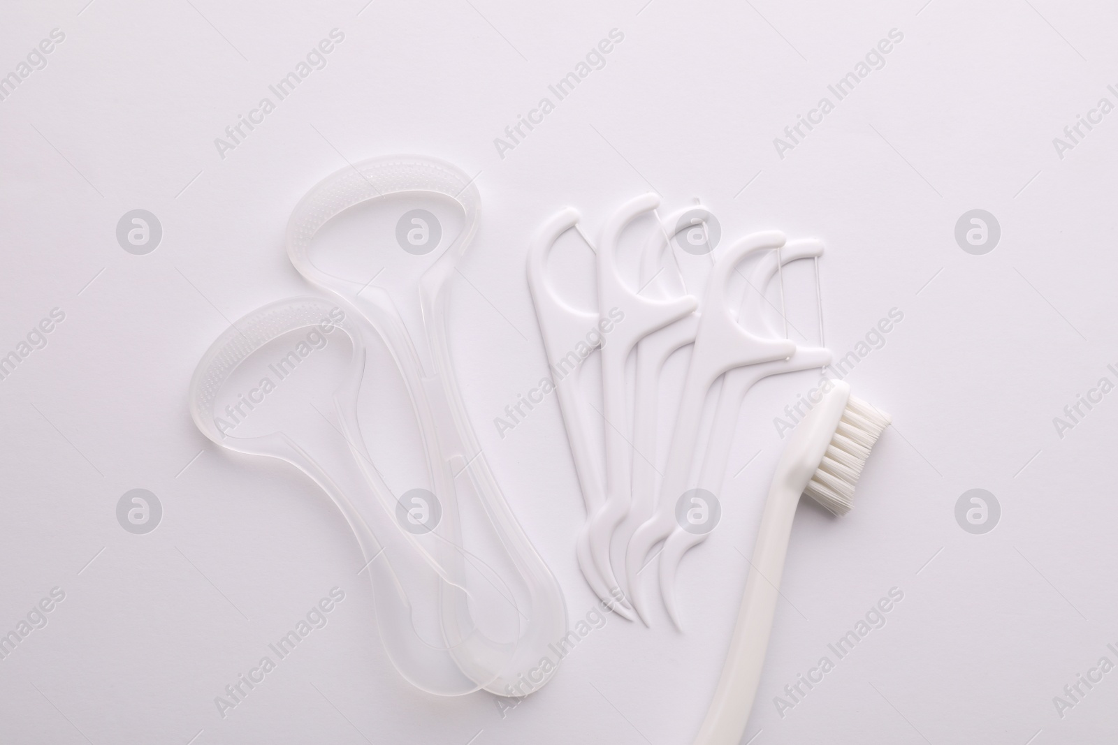 Photo of Tongue cleaners, dental floss picks and toothbrush on white background, top view