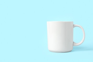 Photo of One white ceramic mug on light blue background, space for text