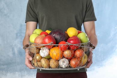 Photo of Man holding basket full of fresh  vegetables and fruits against color background, closeup