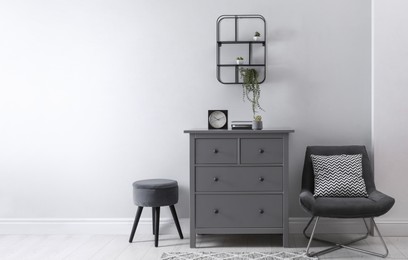 Elegant room interior with stylish chest of drawers, pouf and comfortable armchair