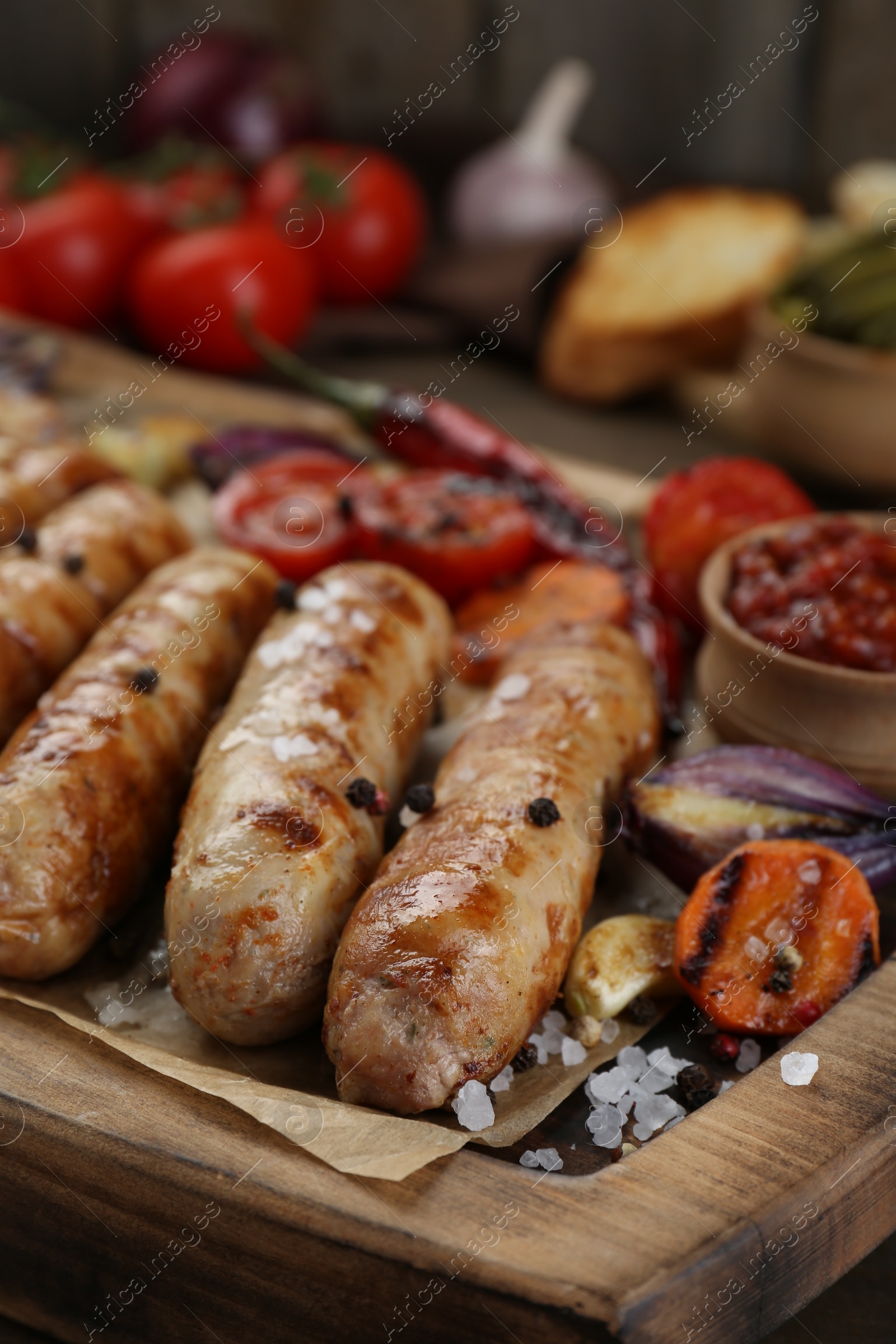 Photo of Tasty grilled sausages with vegetables on wooden board, closeup