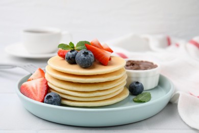 Photo of Delicious pancakes with strawberries, blueberries and chocolate sauce on light table, closeup