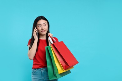 Photo of Beautiful woman with shopping bags talking by smartphone on light blue background. Space for text