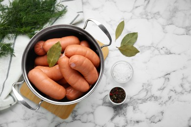 Photo of Pan of delicious sausages, dill, bay leaf, pepper and salt on white marble table, flat lay. Space for text