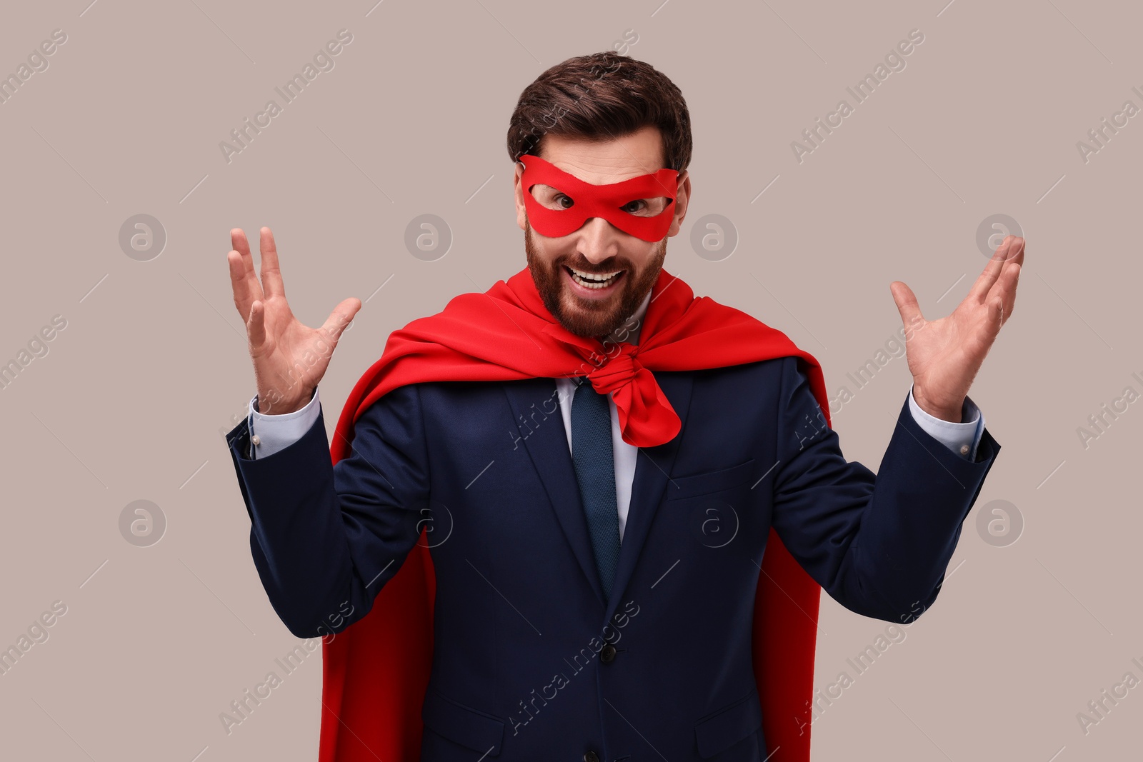 Photo of Happy businessman wearing red superhero cape and mask on beige background