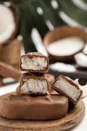 Delicious milk chocolate candy bars with coconut filling on white wooden table, closeup. Space for text