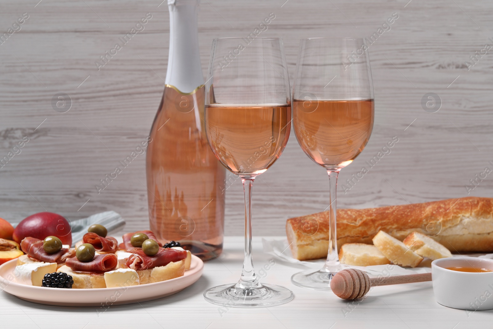 Photo of Delicious rose wine and snacks on white wooden table