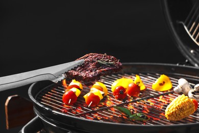 Tongs with tasty steak near modern barbecue grill