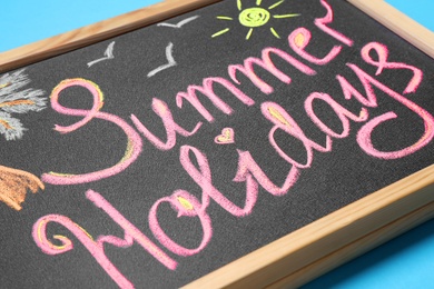 Chalkboard with phrase SUMMER HOLIDAYS on blue background, closeup. School's out