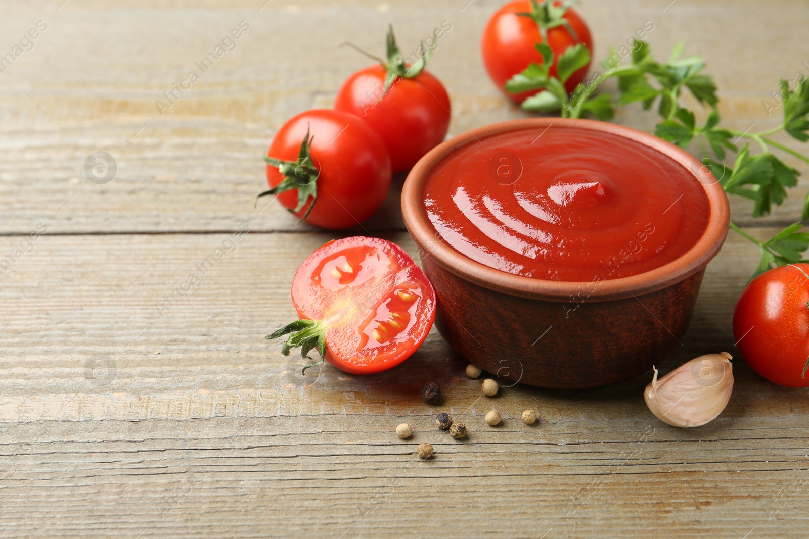 Photo of Tasty ketchup, fresh tomatoes, parsley and spices on wooden table. Space for text