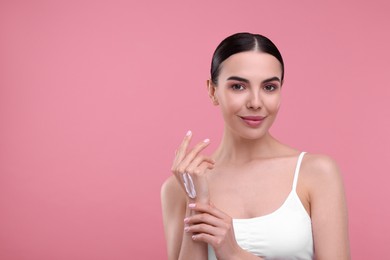 Photo of Beautiful woman with smear of body cream on her hand against pink background, space for text