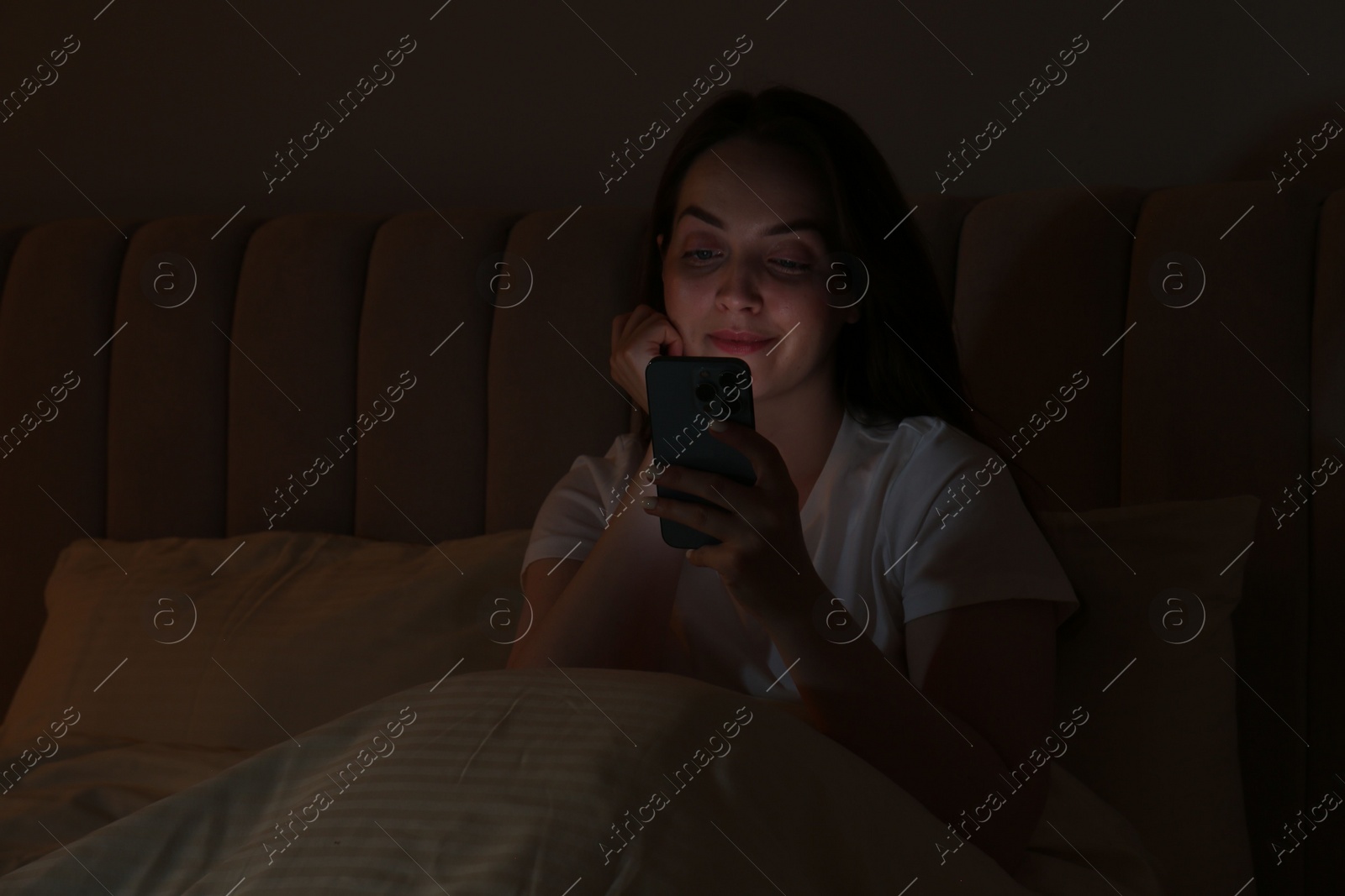 Photo of Woman using smartphone in bed at night. Internet addiction