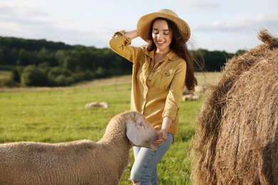 Photo of Smiling woman feeding sheep near hay bale on animal farm