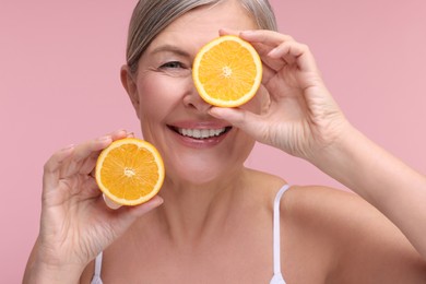 Beautiful woman with halves of orange rich in vitamin C on pink background