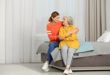 Photo of Elderly woman with female caregiver in bedroom. Space for text