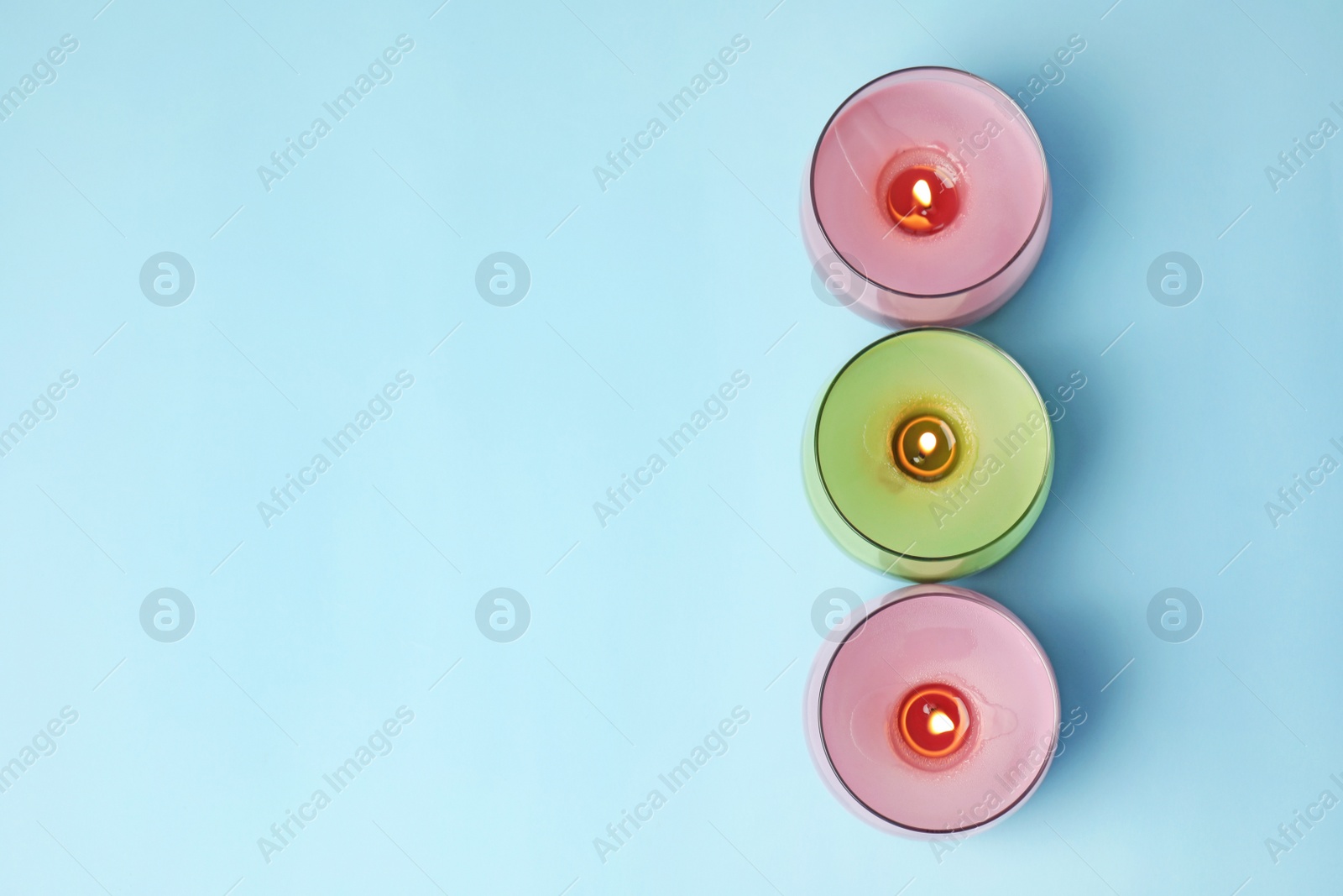 Photo of Burning wax candles in glass holders on light blue background, flat lay. Space for text