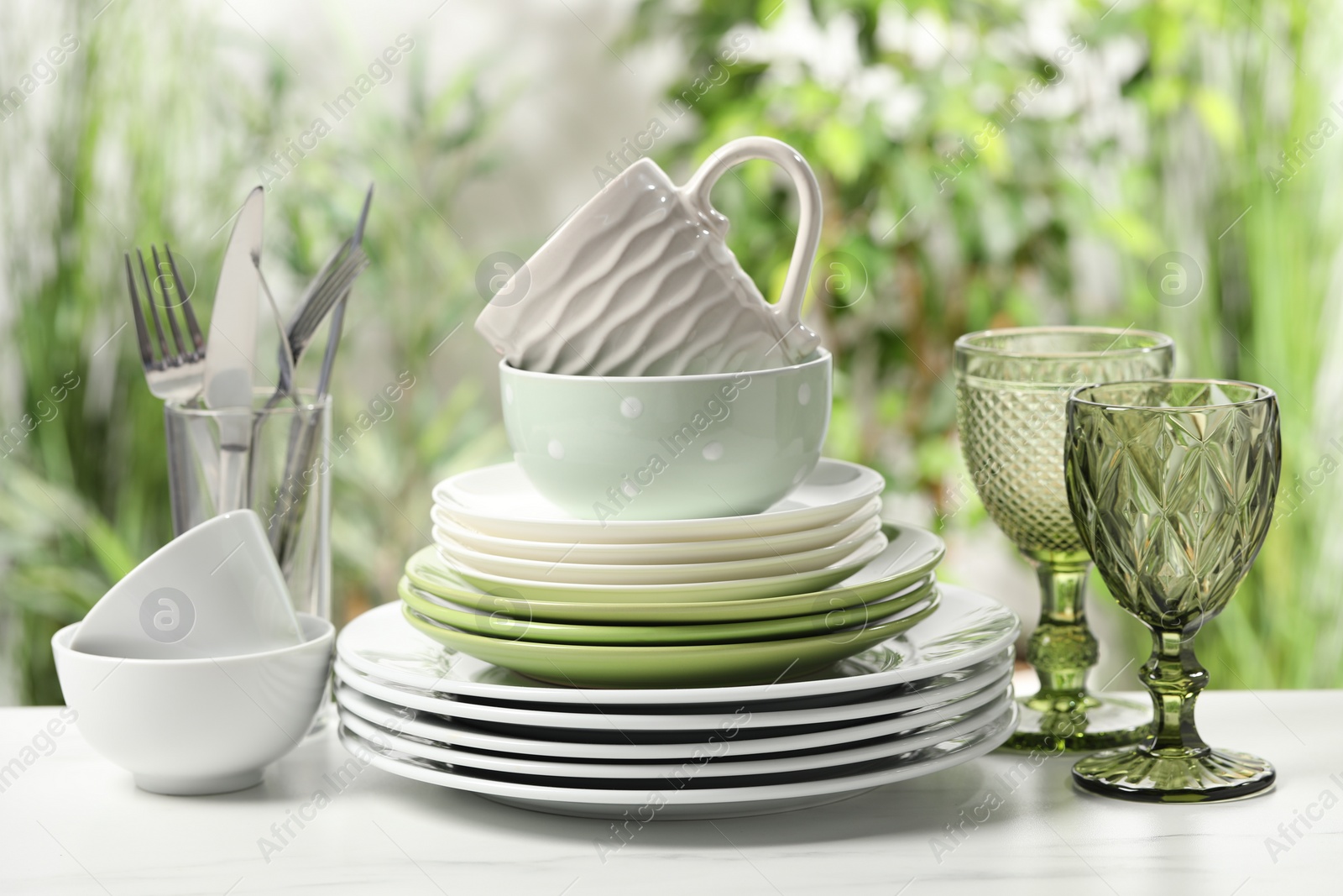 Photo of Beautiful ceramic dishware, glasses, cutlery and cup on white marble table outdoors