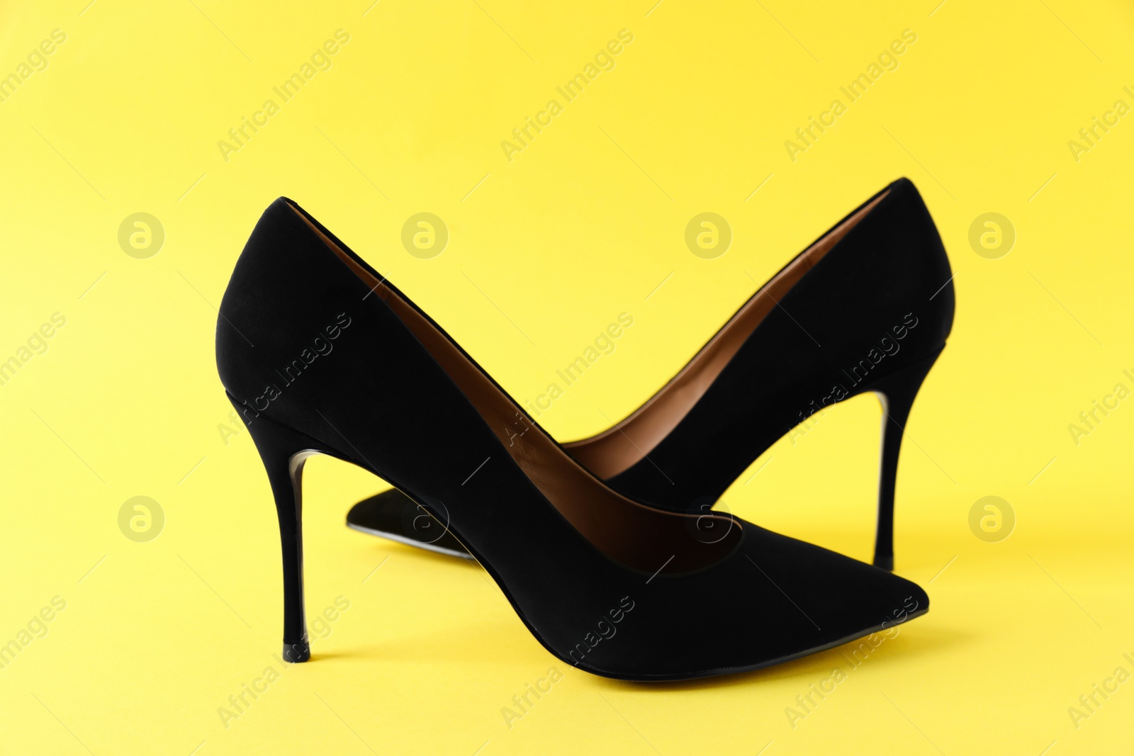 Photo of Pair of elegant black high heel shoes on yellow background