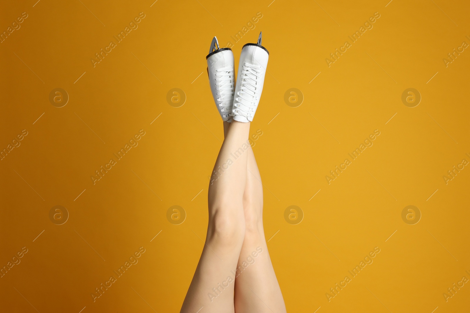 Photo of Woman in elegant white ice skates on yellow background, closeup of legs