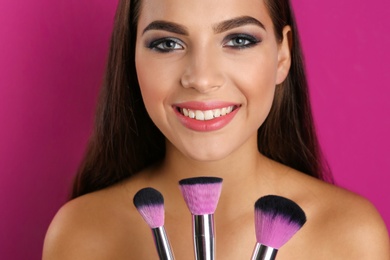 Photo of Portrait of beautiful woman with makeup brushes on color background