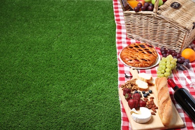 Wicker picnic basket and products on checkered blanket, space for text