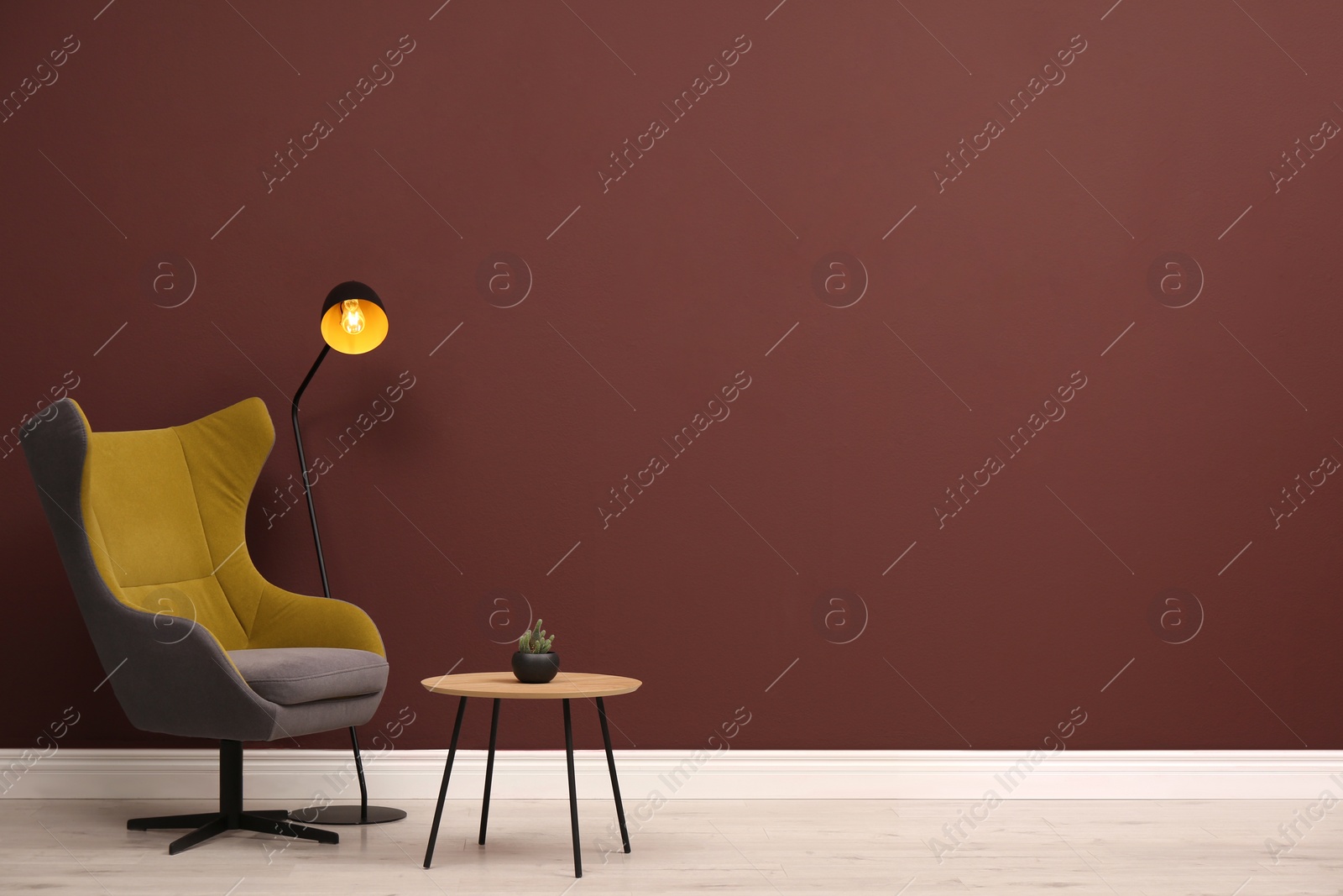 Photo of Stylish armchair, table and lamp near brown wall, space for text