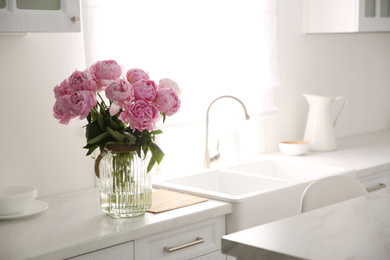 Vase with bouquet of beautiful pink peonies in kitchen. Space for text