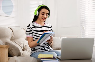 Photo of Young woman writing down notes during webinar at home