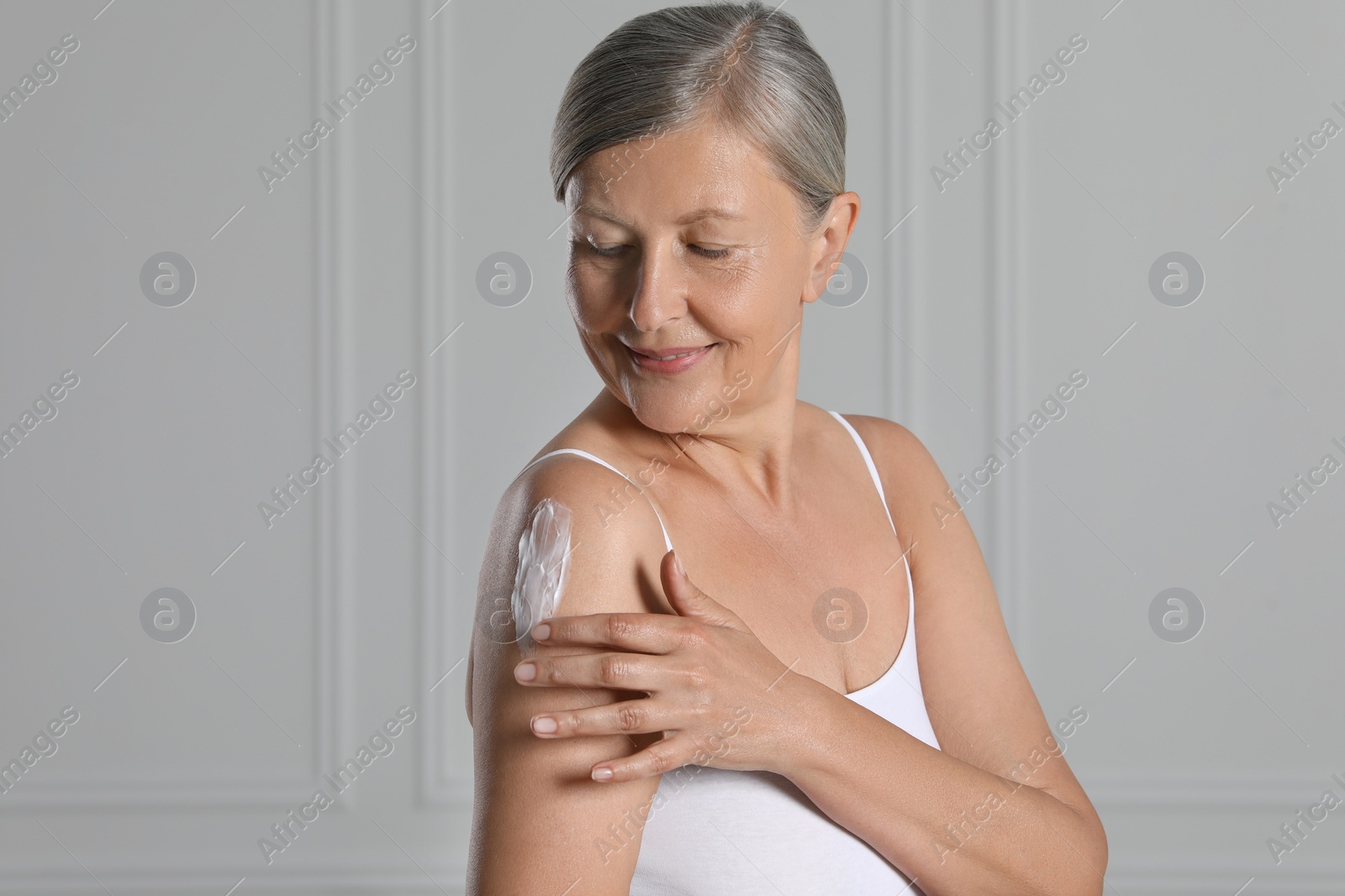 Photo of Happy woman applying body cream on shoulder near white wall