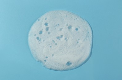 Sample of cleansing foam on light blue background, top view. Cosmetic product