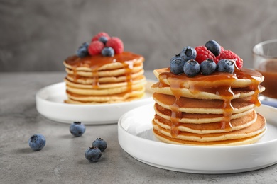 Delicious pancakes with fresh berries and syrup on grey table