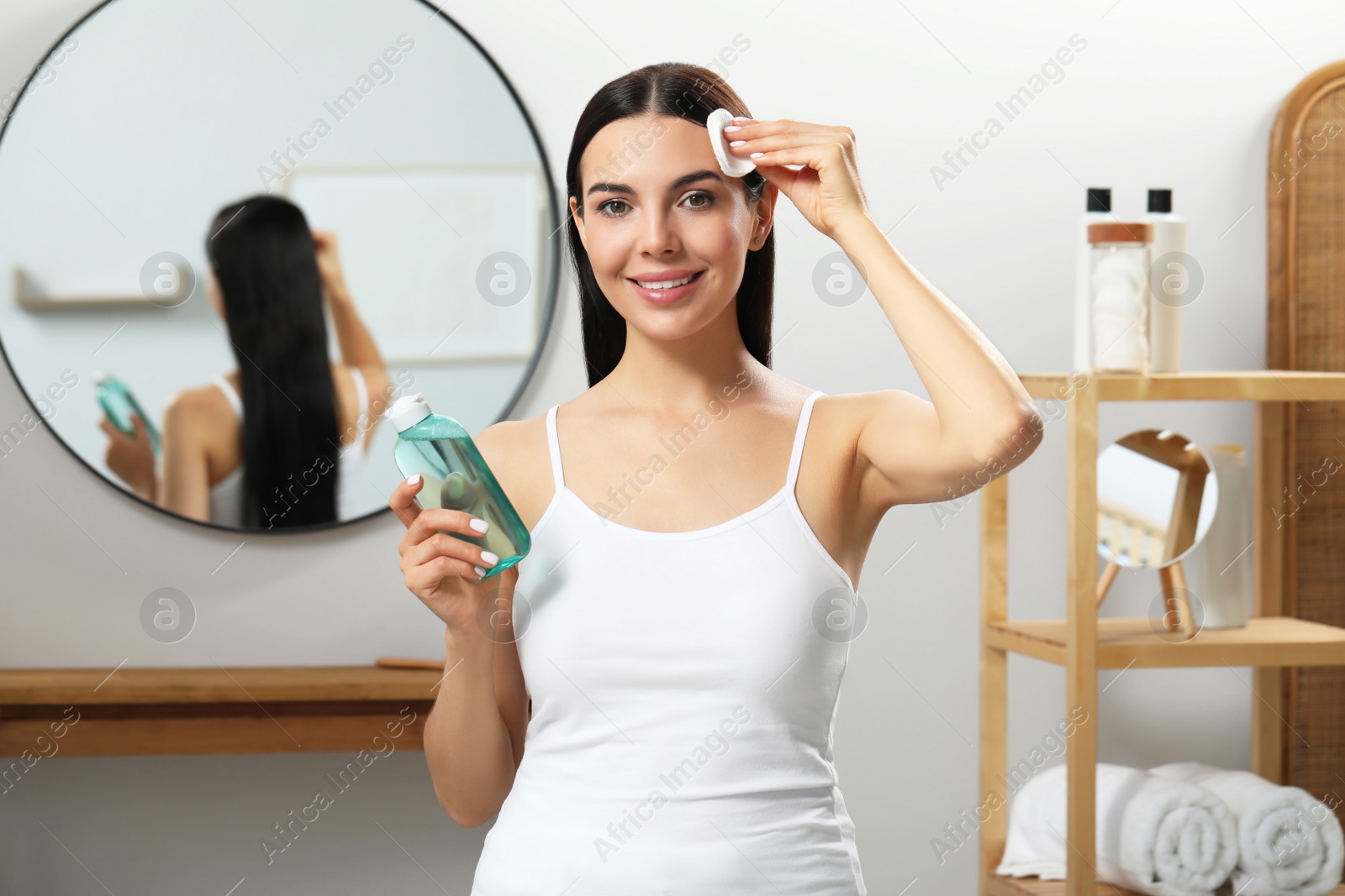 Photo of Young woman using cotton pad with micellar water indoors