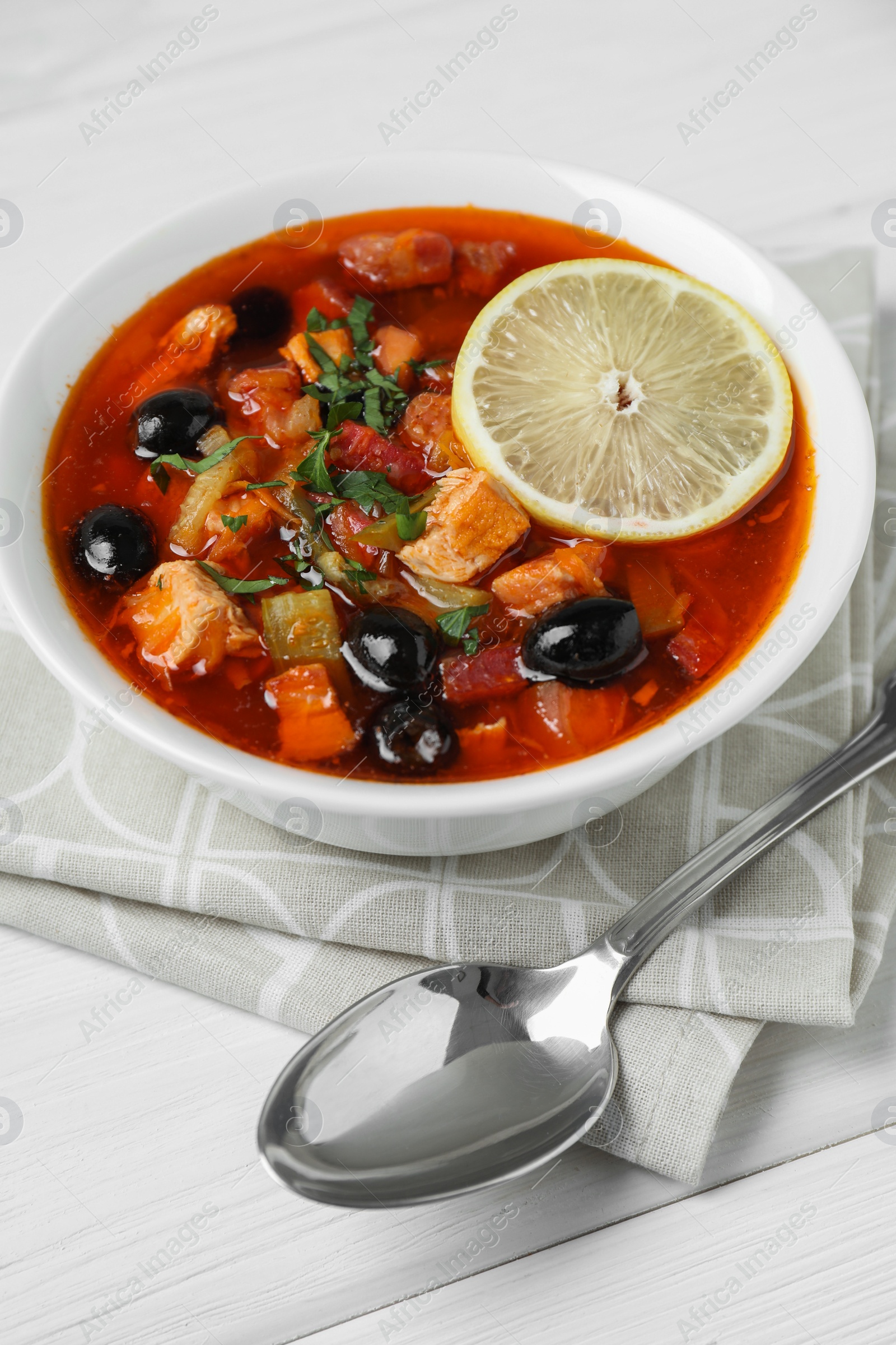 Photo of Meat solyanka soup with sausages, olives, vegetables and spoon on white wooden table