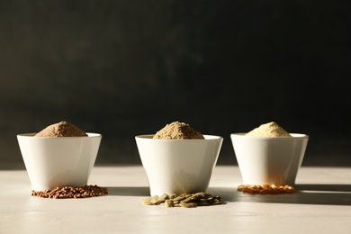 Bowls with different types of flour and seeds on table against dark background. Space for text