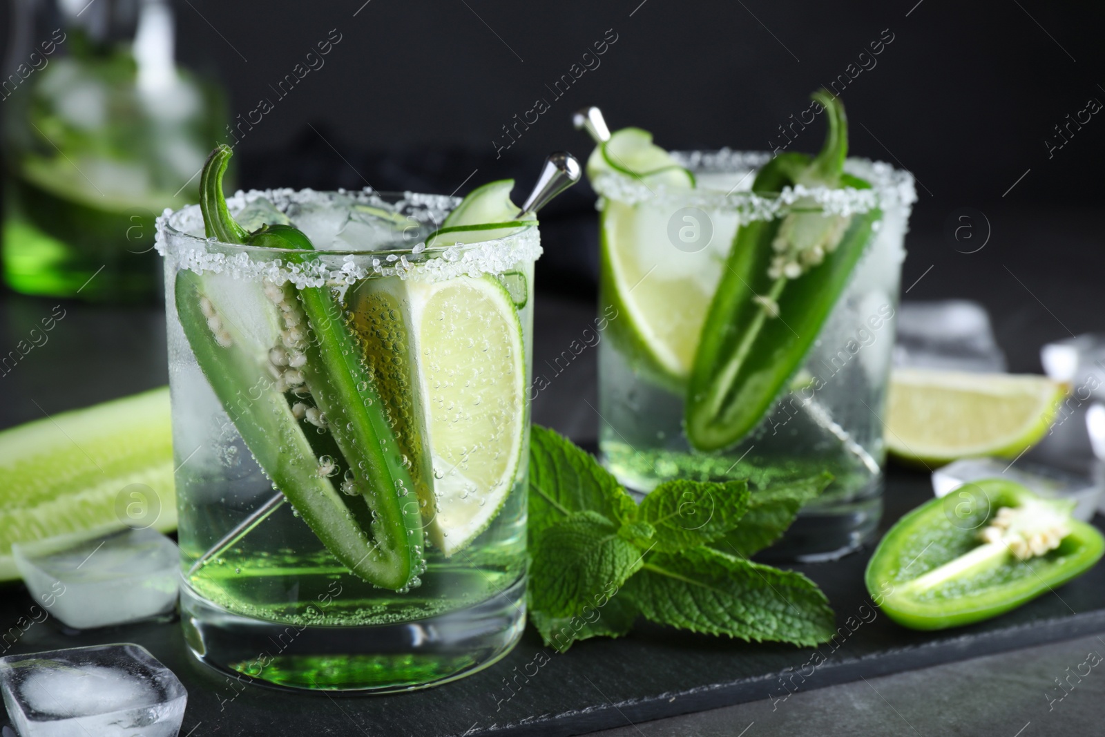 Photo of Spicy cocktail with jalapeno, cucumber and lime on black table