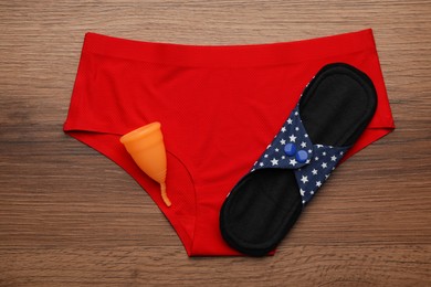Women's underwear, reusable cloth pad and menstrual cup on wooden table, top view