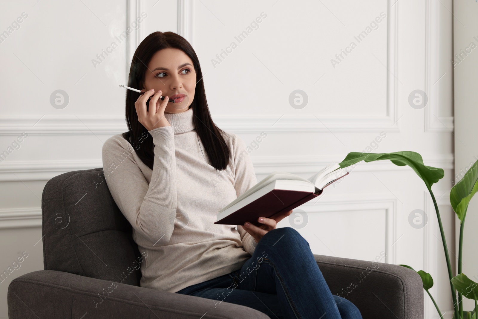 Photo of Woman using cigarette holder for smoking while reading book indoors