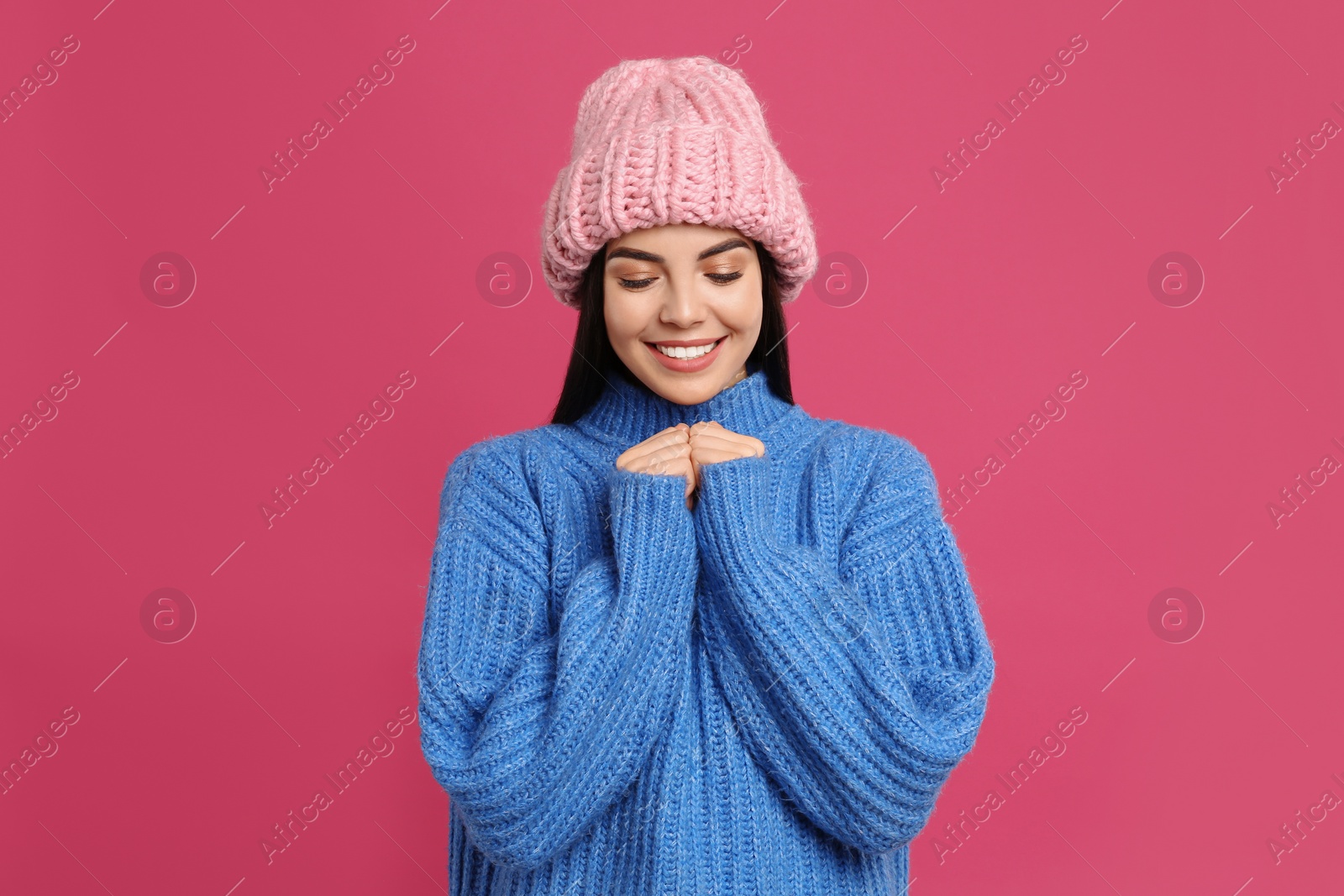 Photo of Young woman wearing warm sweater and hat on crimson background. Winter season