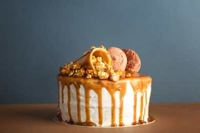 Photo of Delicious homemade cake with caramel sauce and popcorn on table against color background