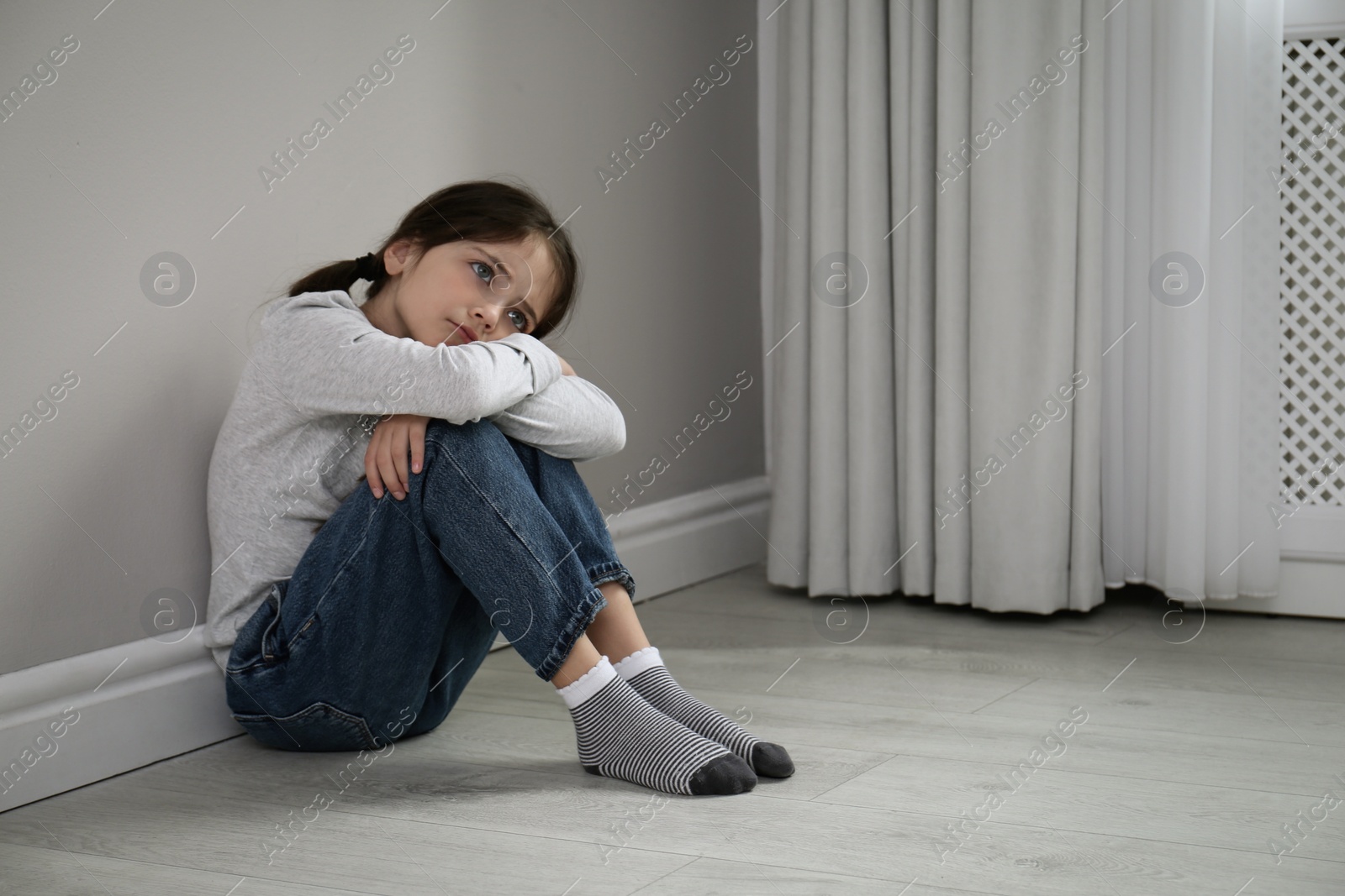 Photo of Sad little girl sitting on floor indoors, space for text