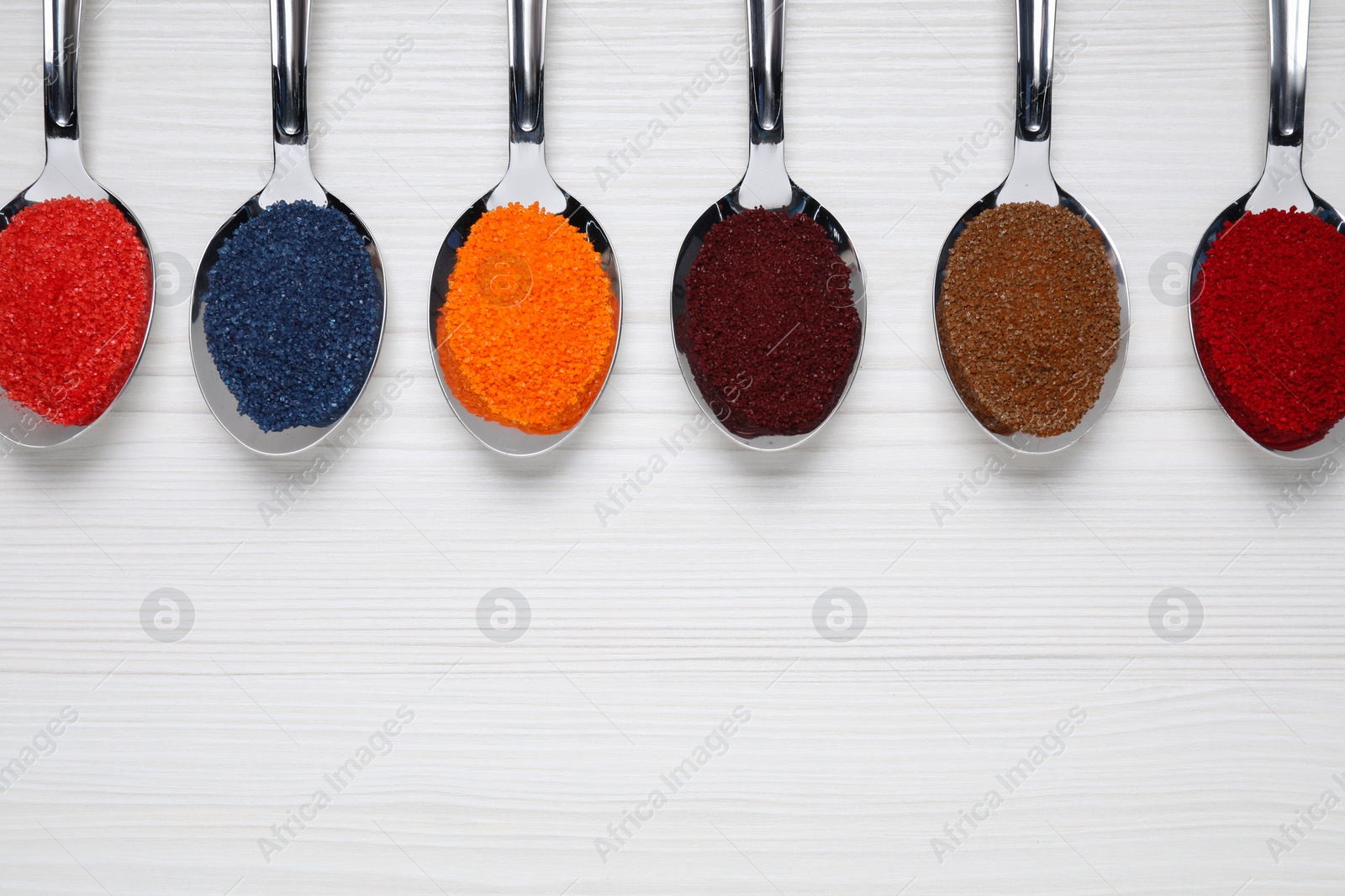 Photo of Spoons with different food coloring on white wooden table, flat lay. Space for text