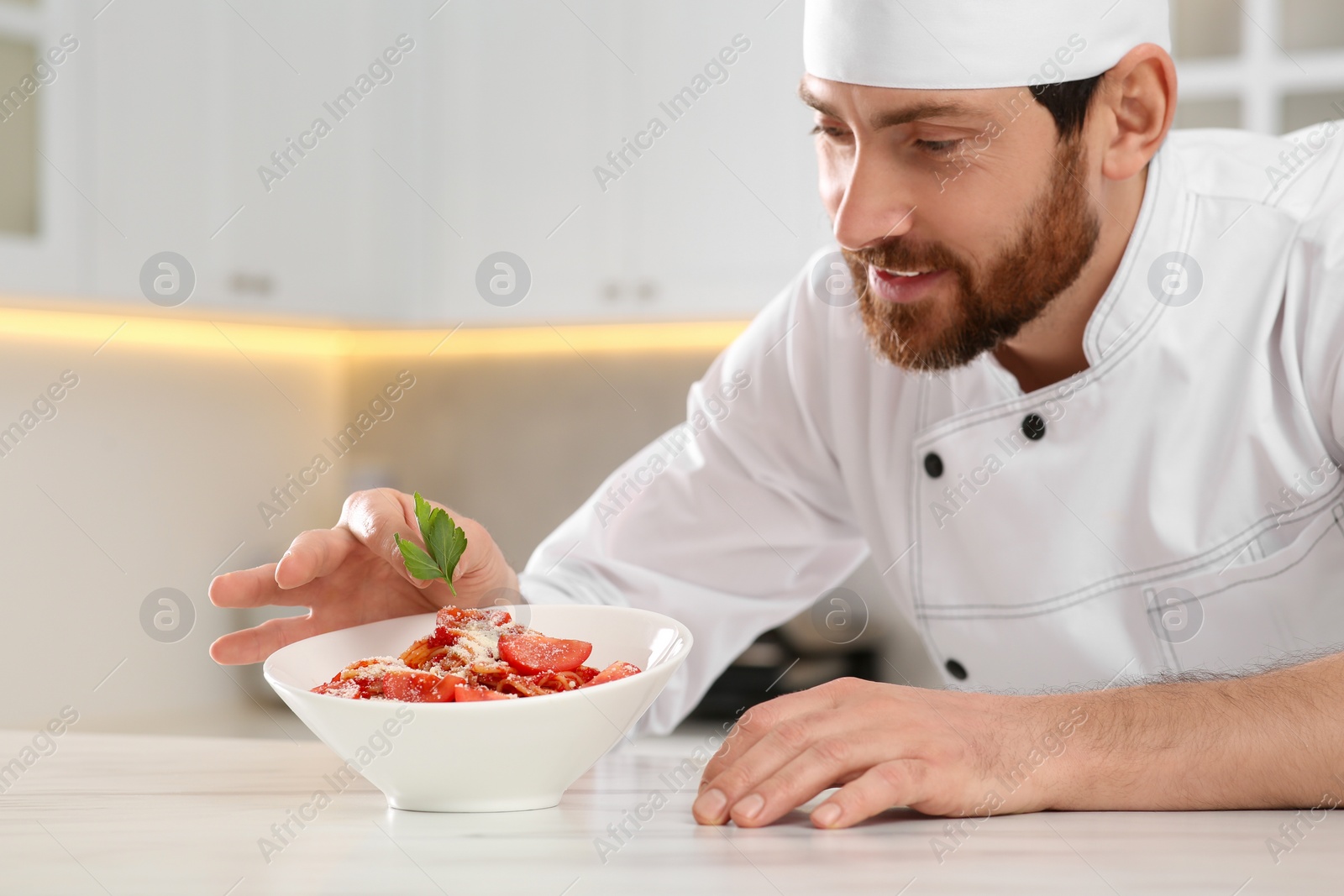 Photo of Professional chef decorating delicious spaghetti with parsley at marble table. Space for text