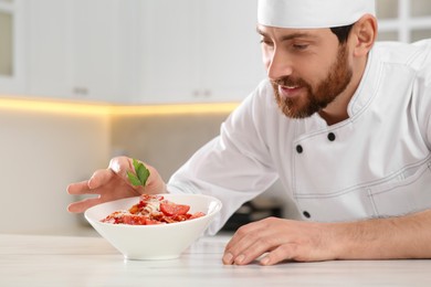 Professional chef decorating delicious spaghetti with parsley at marble table. Space for text