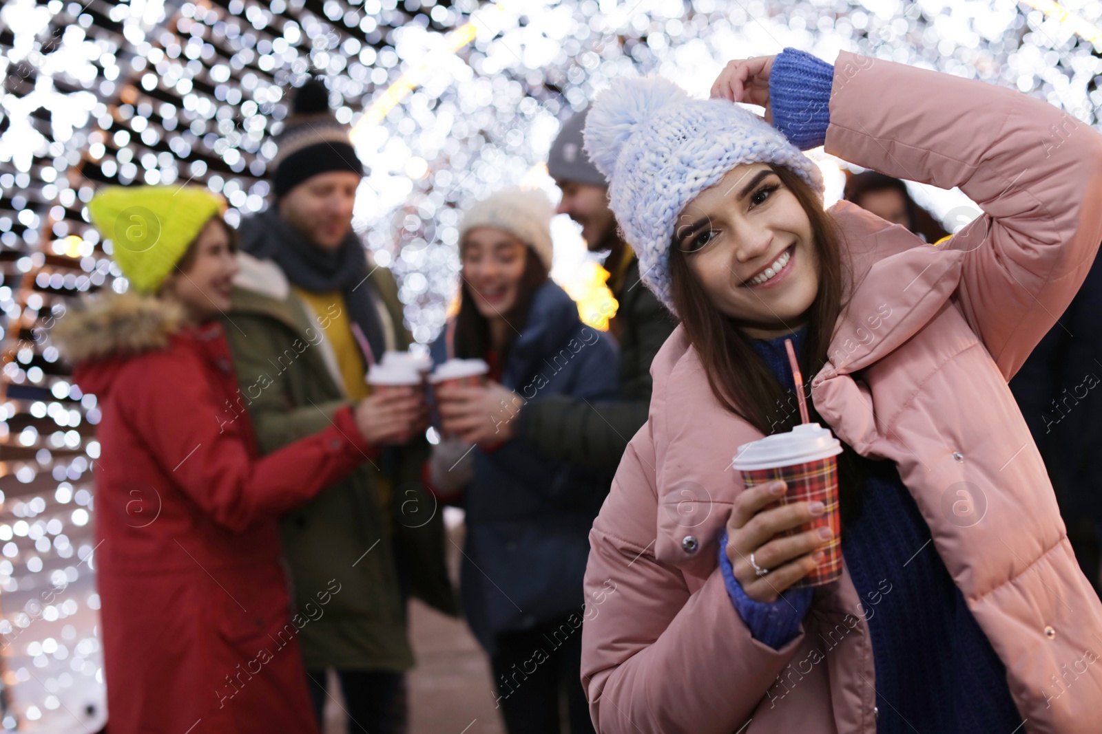 Photo of Happy woman with cup of mulled wine and friends at winter fair. Space for text