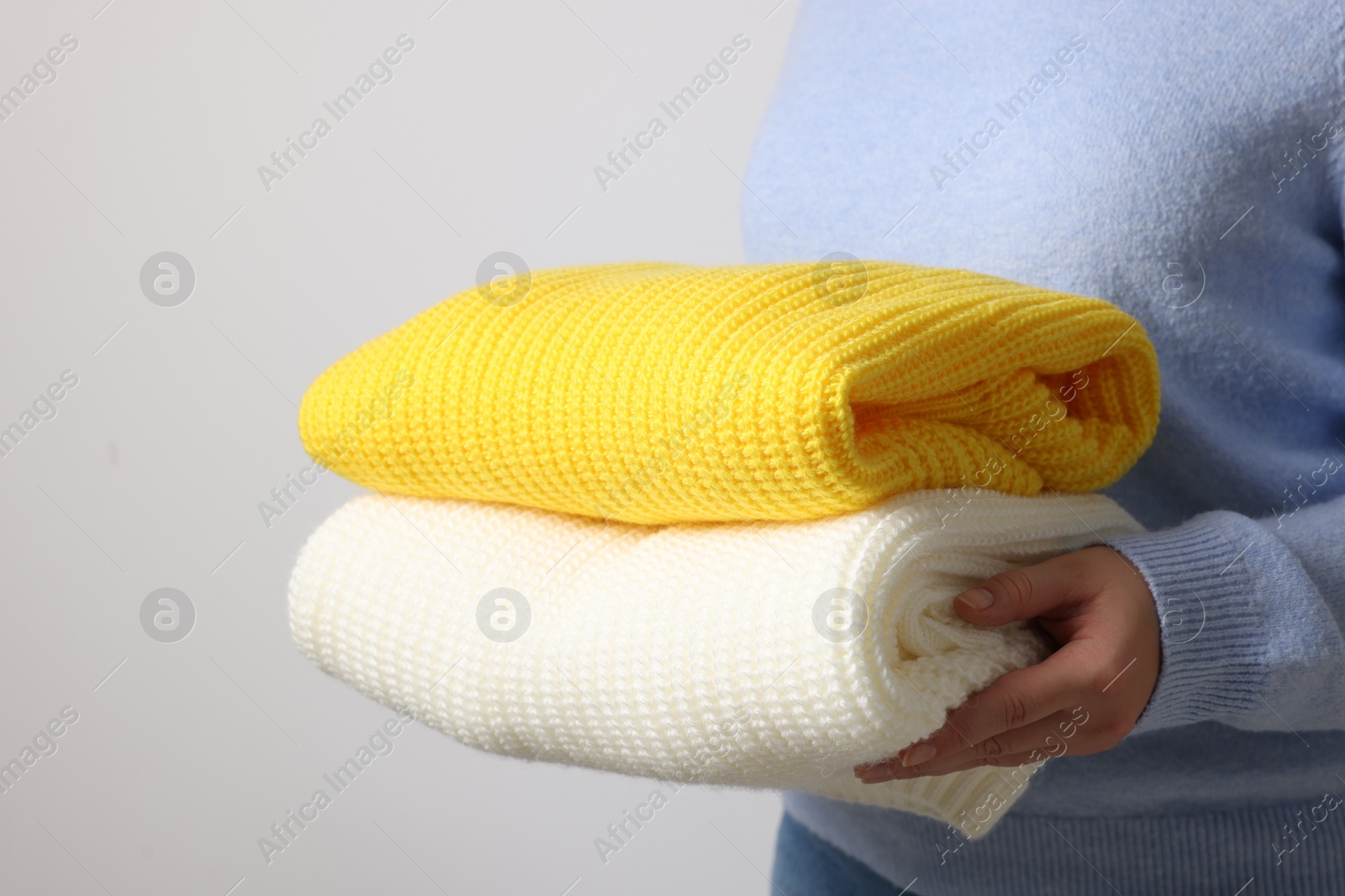 Photo of Woman with knitted sweaters on light background, closeup