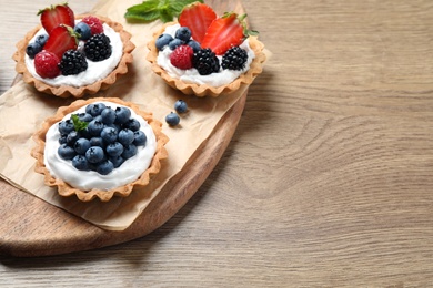 Photo of Different berry tarts on wooden table, space for text. Delicious pastries