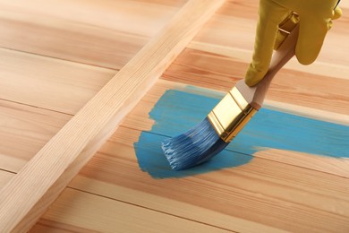 Photo of Worker applying blue paint onto wooden surface, closeup