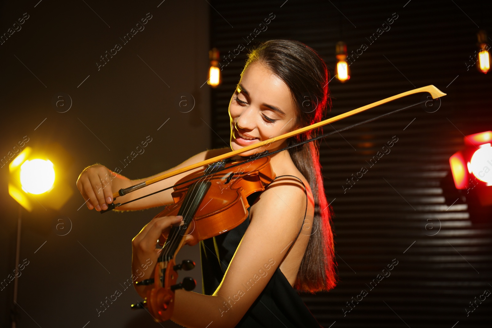 Photo of Beautiful young woman playing violin in dark room